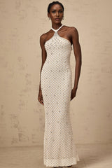 Woman wearing long white halterneck maxi dress with embellished details standing against plain background