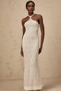Woman wearing long white halterneck maxi dress with embellished details standing against plain background