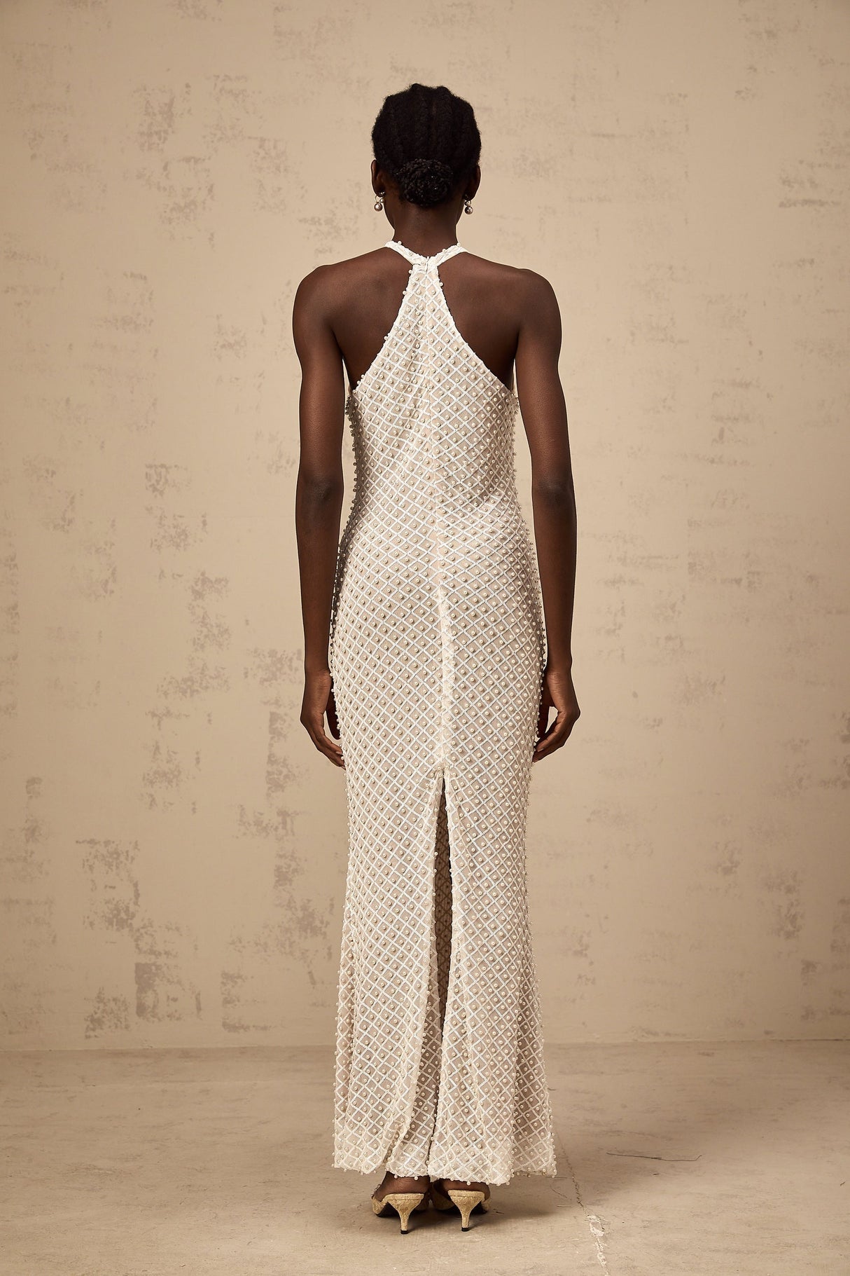 Woman wearing long white halterneck maxi dress with embellished details standing against plain background