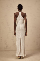 Woman wearing long white halterneck maxi dress with embellished details standing against plain background