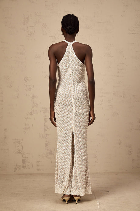 Woman wearing long white halterneck maxi dress with embellished details standing against plain background