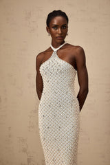 Woman wearing long white halterneck maxi dress with embellished details standing against plain background
