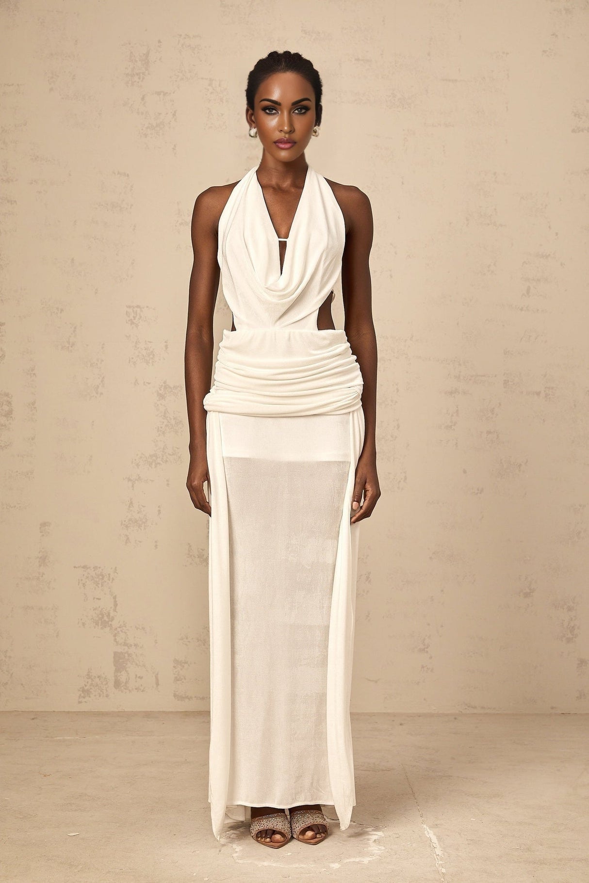 Woman wearing long white halterneck maxi dress with open back standing against plain background