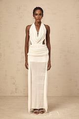 Woman wearing long white halterneck maxi dress with open back standing against plain background