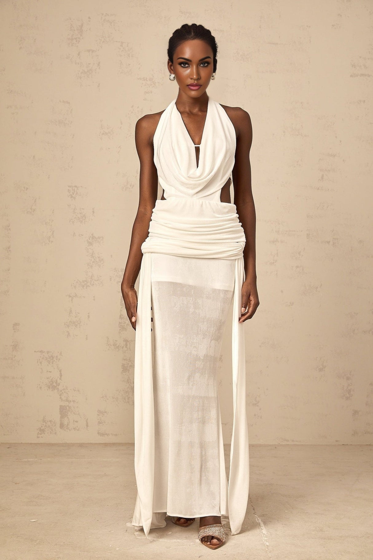 Woman wearing long white halterneck maxi dress with open back standing in front of plain background