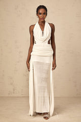 Woman wearing long white halterneck maxi dress with open back standing in front of plain background