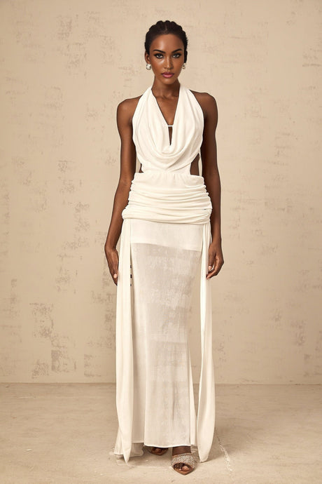Woman wearing long white halterneck maxi dress with open back standing in front of plain background