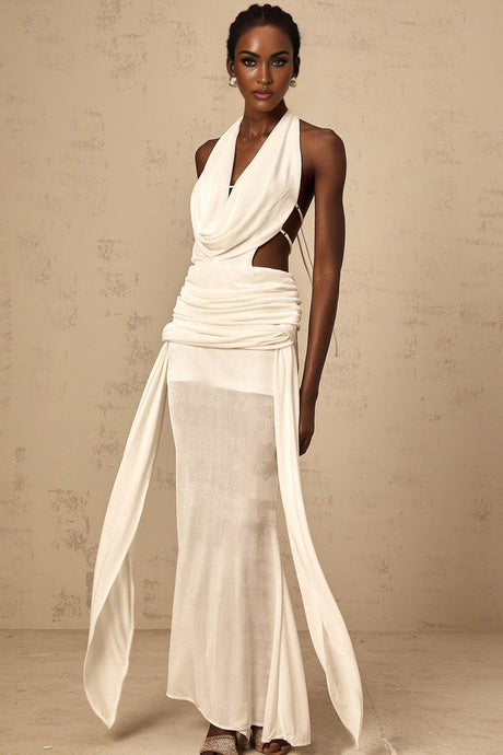 Woman wearing long white halterneck maxi dress with open back standing in sunlit outdoor setting
