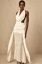 Woman wearing long white halterneck maxi dress with open back standing in sunlit outdoor setting