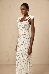 Woman wearing long white maxi dress with colorful floral embroidery pattern standing outdoors