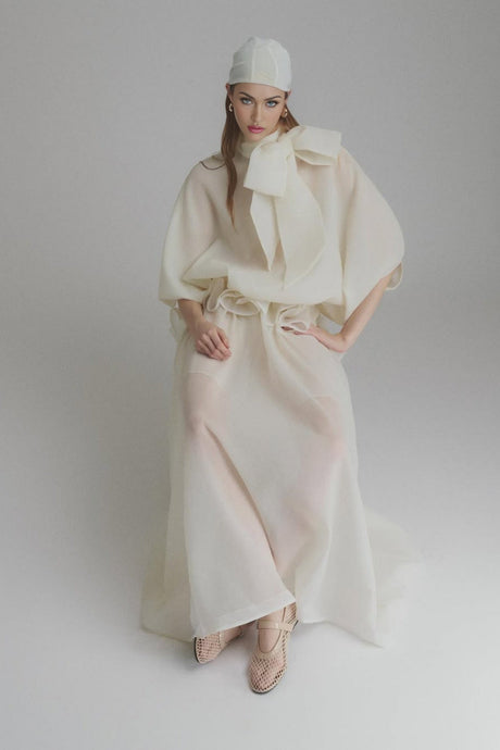 Woman wearing long white maxi dress with ruffled details and tie neck standing in outdoor setting