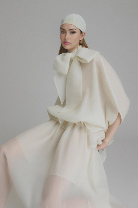 Woman wearing long white maxi dress with tie neck and ruffled details standing in relaxed pose