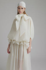 Woman wearing long white maxi dress with tie neck and ruffled details