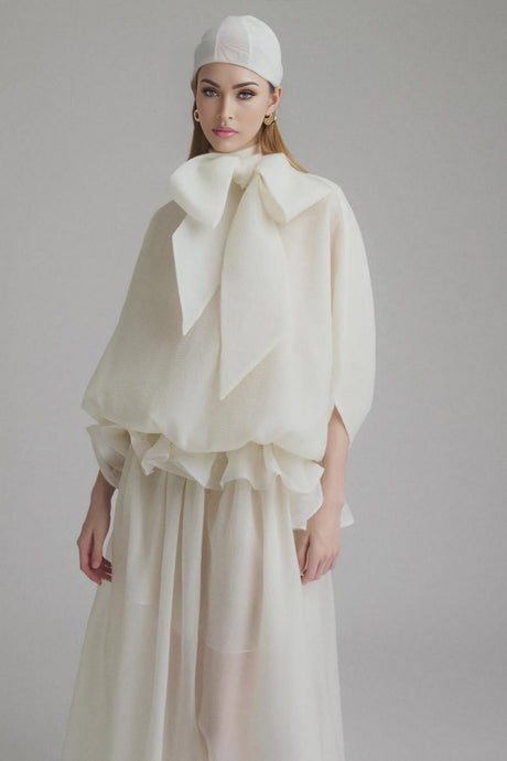 Woman wearing long white maxi dress with tie neck and ruffled details