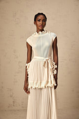 Woman wearing long white sleeveless maxi dress with ruffle details and pleated skirt