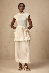 Woman wearing long white sleeveless maxi dress with ruffle details and pleated skirt