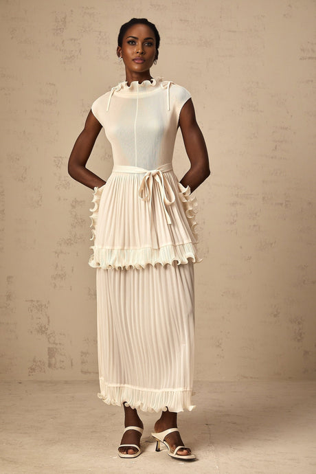 Woman wearing long white sleeveless maxi dress with ruffle details and pleated skirt