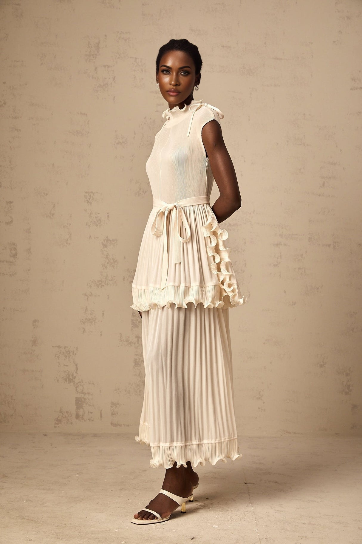 Woman wearing long white sleeveless maxi dress with ruffle details and pleated skirt