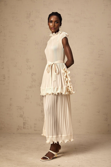 Woman wearing long white sleeveless maxi dress with ruffle details and pleated skirt