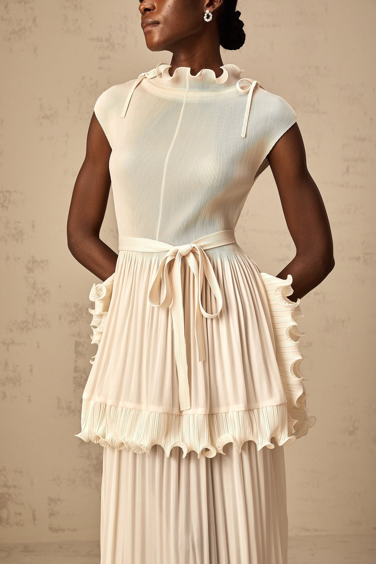Woman wearing long white sleeveless maxi dress with ruffle details and pleated skirt