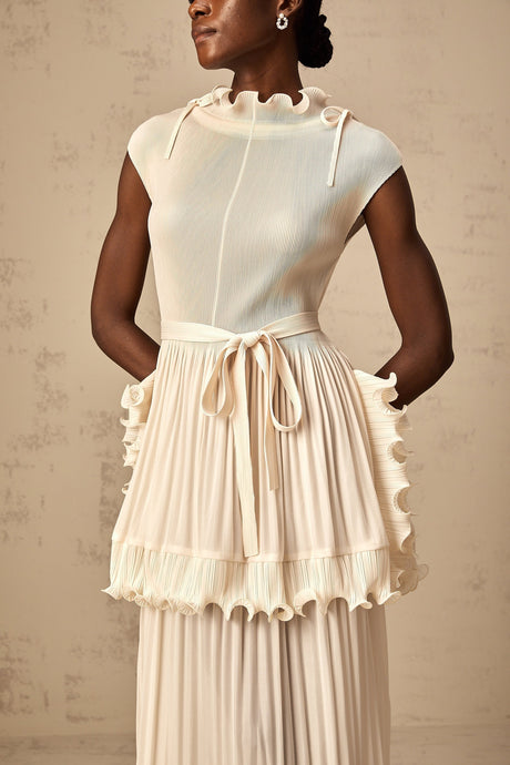 Woman wearing long white sleeveless maxi dress with ruffle details and pleated skirt