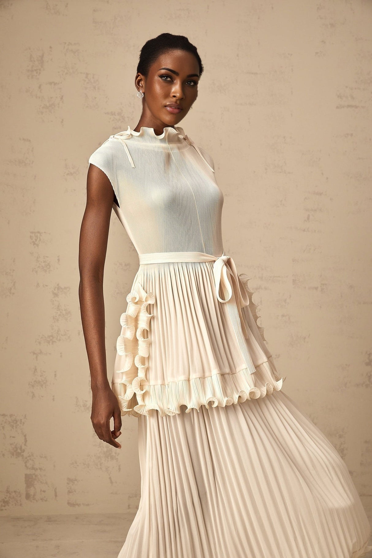 Woman wearing long white sleeveless maxi dress with ruffle details and pleated skirt