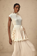 Woman wearing long white sleeveless maxi dress with ruffle details and pleated skirt