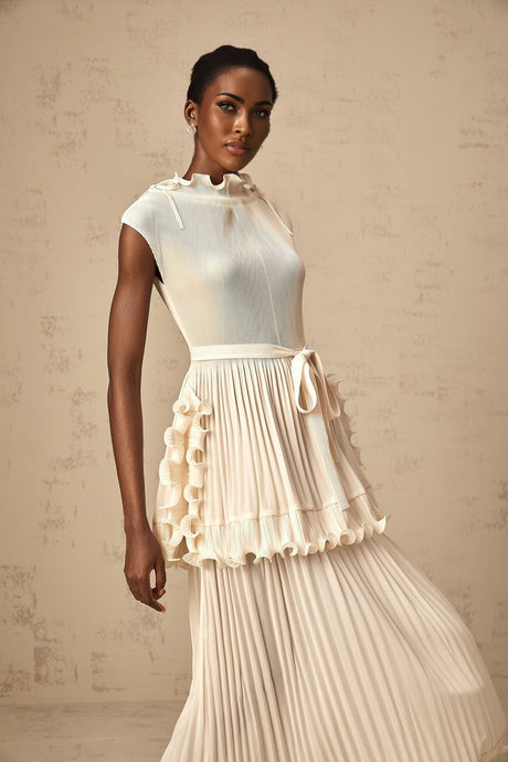 Woman wearing long white sleeveless maxi dress with ruffle details and pleated skirt