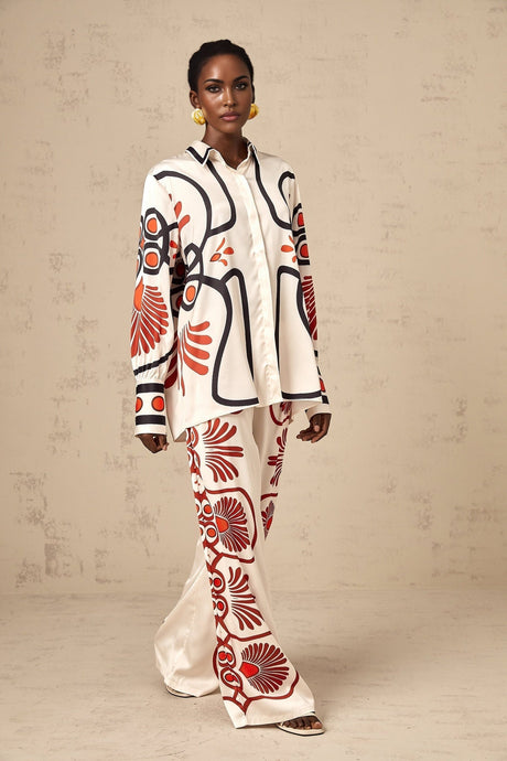 Woman wearing matching floral print shirt and trousers set in vibrant colors standing against plain background