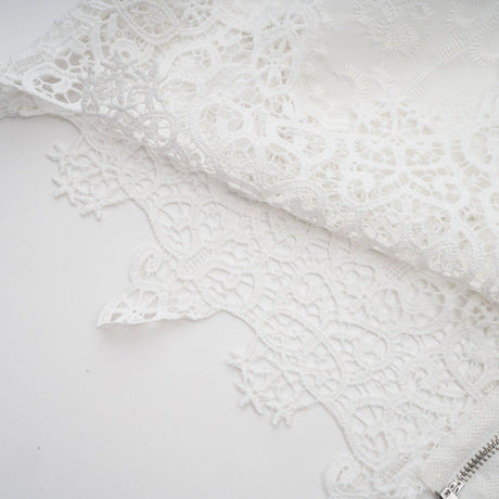 Woman wearing matching white lace trimmed cropped top and trousers set with cutout details