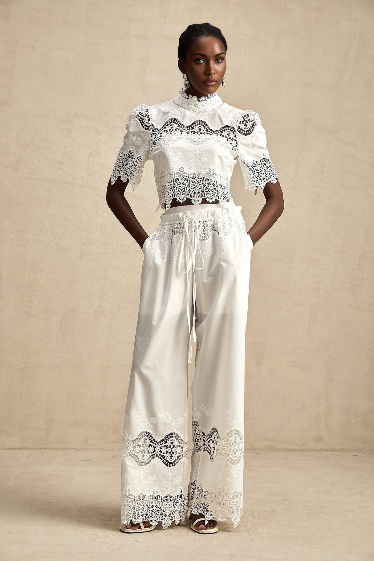 Woman wearing matching white lace trimmed cropped top and trousers set with cutout details