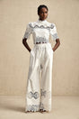 Woman wearing matching white lace trimmed cropped top and trousers set with cutout details