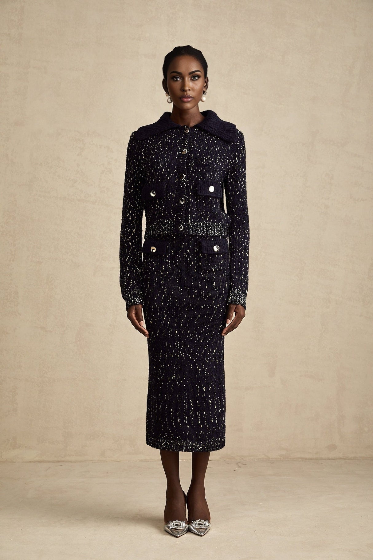 Woman wearing navy blue crochet knit jacket and matching skirt set standing against plain background