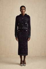 Woman wearing navy blue crochet knit jacket and matching skirt set standing against plain background