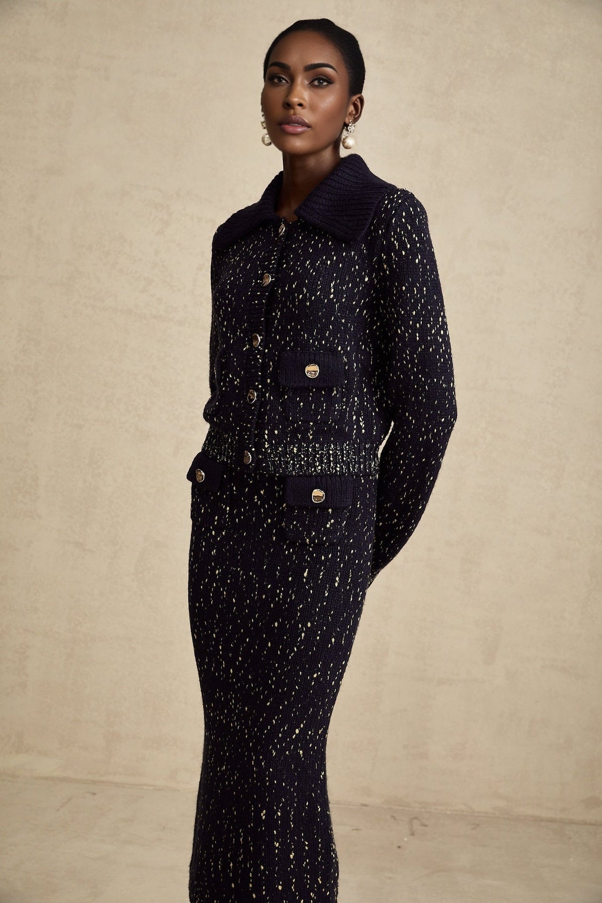Woman wearing navy blue crochet knit jacket and matching skirt set standing against white background