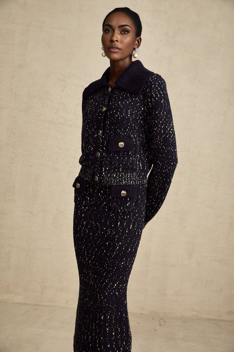Woman wearing navy blue crochet knit jacket and matching skirt set standing against white background