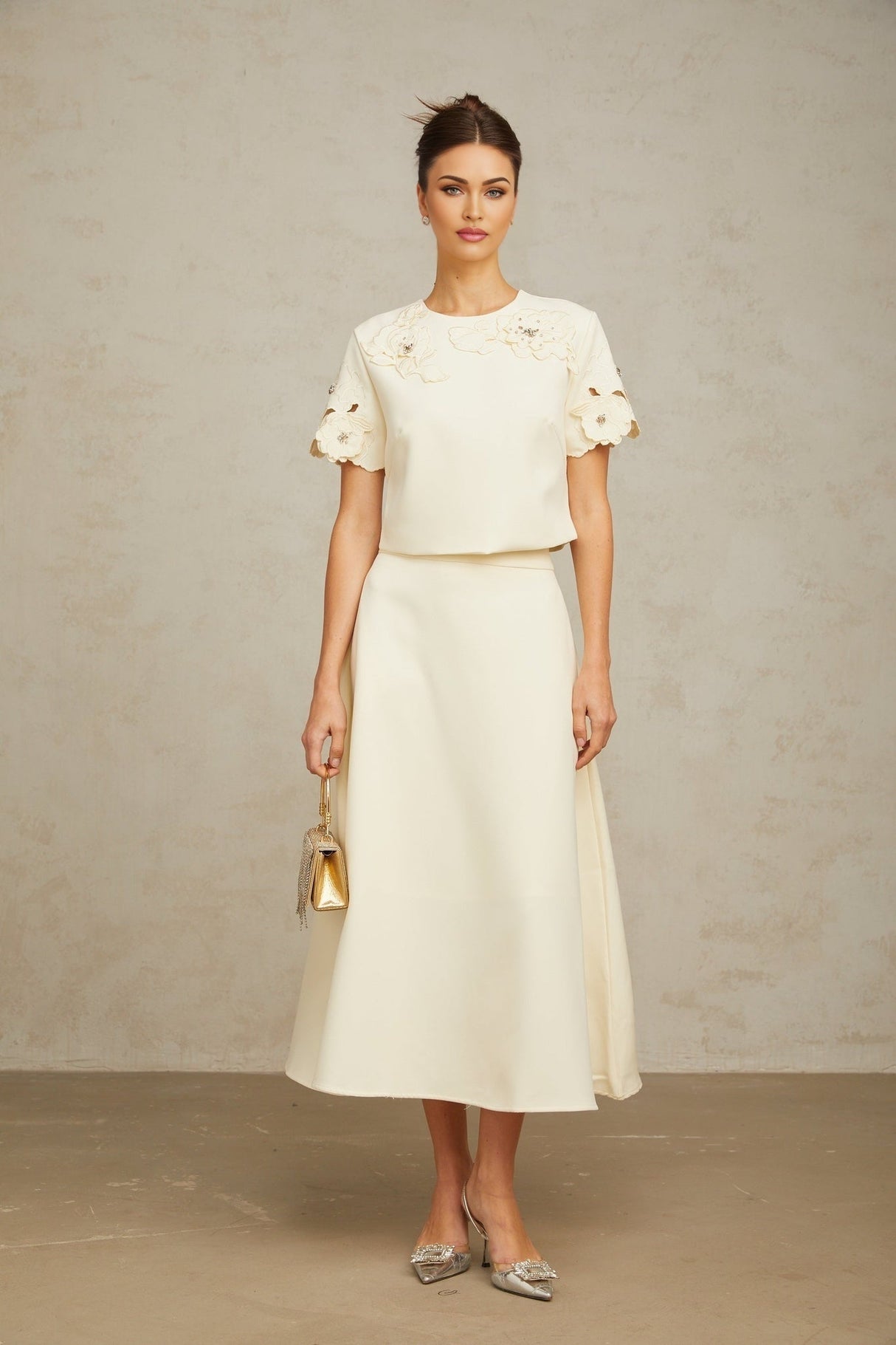 Woman wearing neutral colored matching set with three dimensional petal details on top and skirt