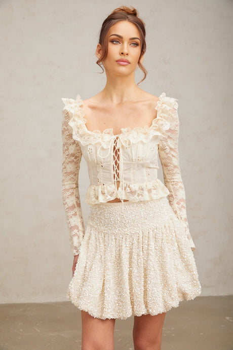 Woman wearing off white floral lace blouse with ruffled details and long sleeves