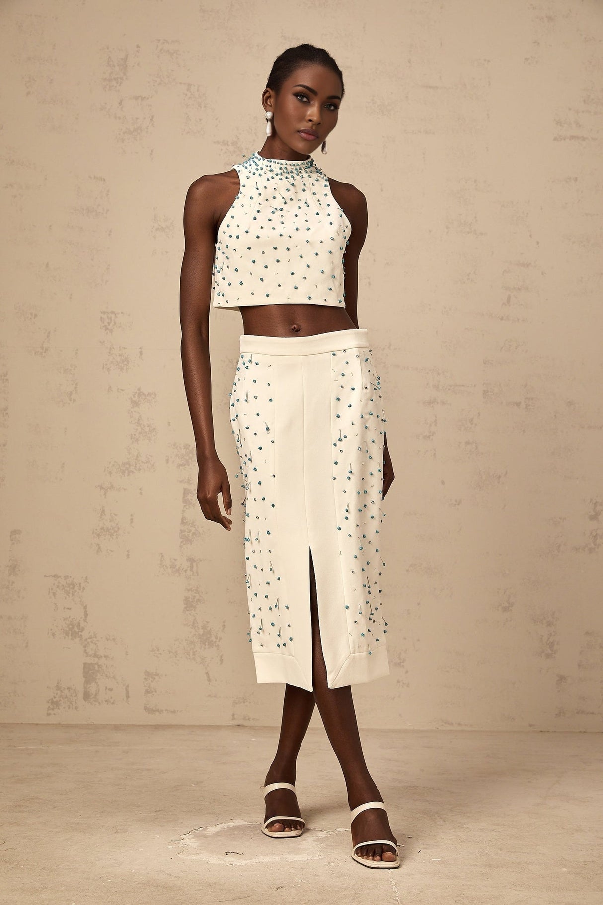 Woman wearing off white two piece outfit consisting of embellished top and matching skirt