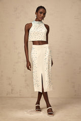 Woman wearing off white two piece outfit consisting of embellished top and matching skirt