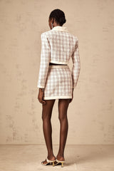 Woman wearing pink checked tweed jacket and matching skirt set standing against plain background