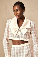 Woman wearing pink checked tweed jacket and matching skirt set standing against plain background