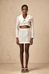 Woman wearing pink checked tweed jacket and matching skirt set standing against plain background
