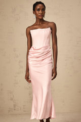 Woman wearing pink offshoulder maxi dress with flowing skirt standing in sunlit garden