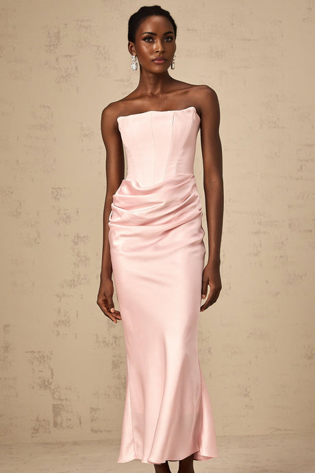 Woman wearing pink offshoulder maxi dress with flowing skirt standing in sunlit garden