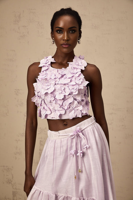Woman wearing purple floral print top and matching skirt set with faux flower design