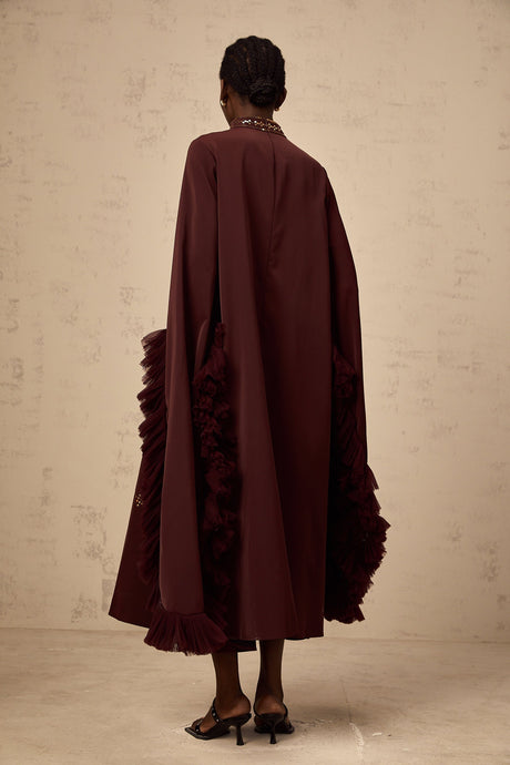 Woman wearing purple sequined midi dress with flared sleeves standing against plain background