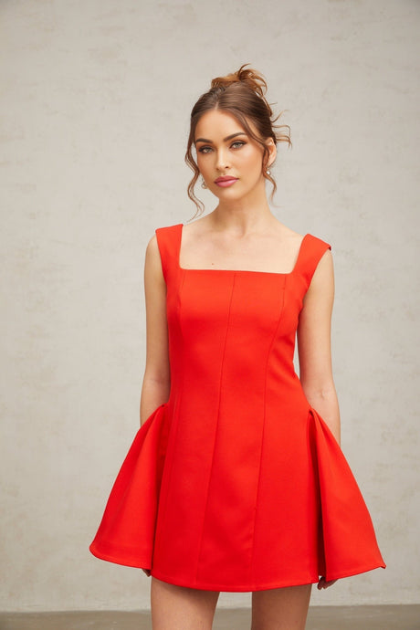 Woman wearing red Margherita mini dress with square neckline and puff sleeves standing against plain background
