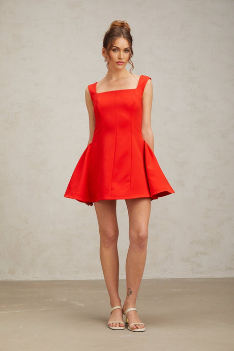 Woman wearing red mini dress with square neckline and puff sleeves standing against plain background