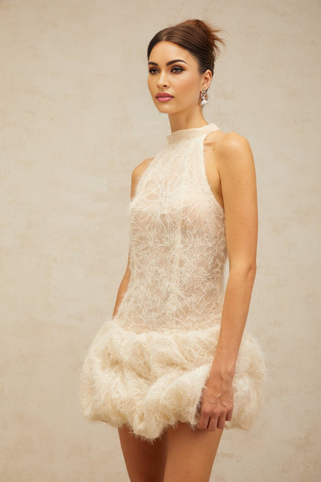 Woman wearing short beige textured mini dress with puff sleeves and gathered fabric details